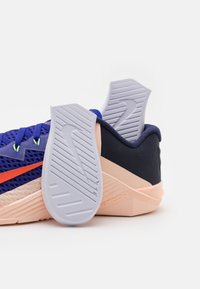 Scarpa atletica in rete blu con suola rosa, accento arancio e battistrada in gomma grigia. Caratterizzata da pannelli testurizzati e lacci.