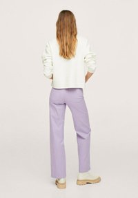 Pull blanc texturé avec des manches retroussées associé à un pantalon lilas clair. Les chaussures présentent une semelle épaisse beige et un dessus lisse.