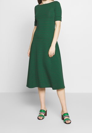 Robe midi rayée verte et noire avec des manches courtes, un col large et une jupe évasée ; assortie à des sandales à talons à lanières noires et vertes.