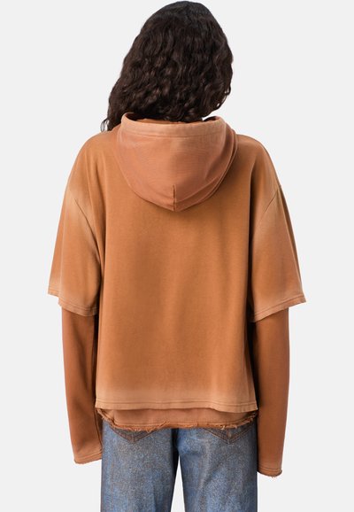 Hoodie marrone oversize con una texture morbida, maniche corte e cappuccio con coulisse. Abbinato a jeans blu con un effetto sbiadito.