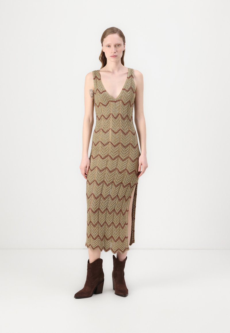 Abito senza maniche a lunghezza ginocchio con motivo a zigzag in oro e bordeaux. La trama della fibra e lo spacco laterale arricchiscono il design. Stivali da cowboy marroni.