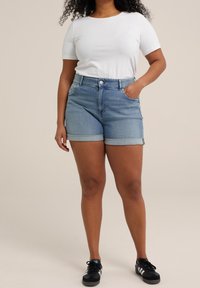 Ljust blå denimshorts med uppvikt fåll, med framfickor och bältesöglor. Matchat med en åtsittande vit kortärmad skjorta.