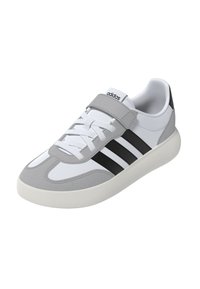 Sneaker bianca con accenti grigi, caratterizzata da una parte superiore liscia simile alla pelle, strisce nere e una fascia in velcro sopra i lacci tradizionali.