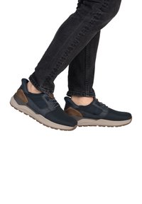 Baskets bleu marine avec un dessus texturé, accents marron sur le talon et une semelle gris clair. Comprend des lacets et un col rembourré pour un meilleur maintien.