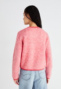 Rozā svītrains džemperis ar brīvu piegriezumu, ar apaļu kakla izgriezumu un ribu struktūru. Aizmugures skats rāda nolaistas plecus un īsu garumu.