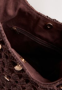 Brown woven handbag with gold shell and starfish charms, showing interior fabric lining and a small zippered pocket.