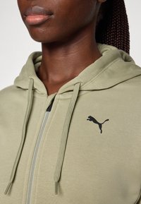 Ljusgrön zip-up hoodie med dragsnören och en svart Puma-logotyp. Har en mjuk textur och en design med känguruficka.