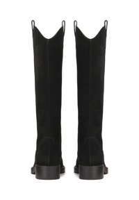Botas negras de ante hasta la rodilla con un borde superior puntiagudo, que cuentan con dos tiradores y un tacón bajo apilado.