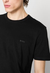 Čierne tričko s krátkym rukávom vyrobené z jemnej látky, s okrúhlym výstrihom a diskrétnym embosovaným logom "BOSS" na ľavej strane hrudníka.