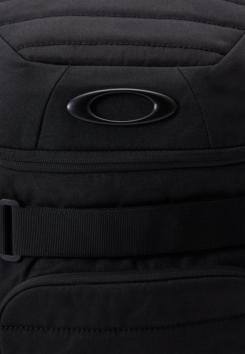 Zaino in tessuto nero con design imbottito, cinturino regolabile e logo rotondo distintivo. Materiale testurizzato con una fibbia resistente.