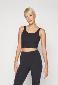 Top crop preto com textura canelada e alças largas, combinado com leggings pretas de cintura alta. Textura suave e design ajustado para vestuário ativo.