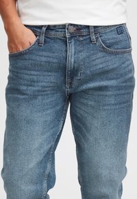 Blå denimjeans med klassisk design med fem fickor, subtila slitningar och kontrasterande sömmar på skarvar och midjeband.