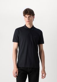 Μαύρο πόλο μπλουζάκι σε λείο, ελαφρύ ύφασμα με κολάρο, κοντά μανίκια και διακριτικό κεντητό λογότυπο στο στήθος.