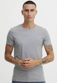 Tricou gri cu mânecă scurtă și guler rotund, realizat dintr-un material moale. Dispune de un design ajustat și o textură netedă, purtat cu blugi bleumarin.