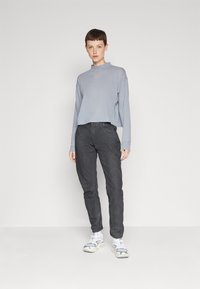Cămașă lungă de un gri deschis, cu guler înalt și design scurt, asociată cu pantaloni strâmți de un gri închis și adidași argintii sport.