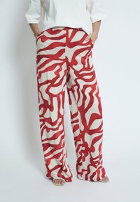 Weite Hosen aus cremigem Stoff mit kräftigem roten abstrakten Muster. Mit seitlichen Taschen und einer entspannten Passform, ideal für den Alltag.