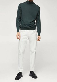 Tumma vihreä poolopaita, joka on yhdistetty valkoisiin kapeisiin housuihin ja mustiin loafereihin, sisältää teksturoitua kangasta ja istuvan tyylin.