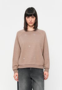 Sweatshirt marron avec un col rond et des manches raglan, orné de décorations florales argentées. Assortis avec un jean gris foncé.