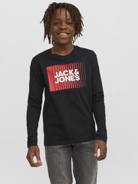 Majica dugih rukava u tamnoplavoj boji sa bijelim i crvenim grafičkim logom koji na prednjoj strani glasi "JACK & JONES"; nosi se uz sive traperice.