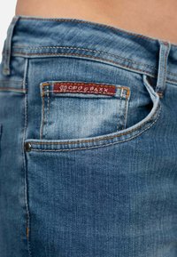 Blauwe denim jeans met een lichte wassing, voorzien van oranje stiksels, een opvallende achterzak en een rode label met de merknaam.
