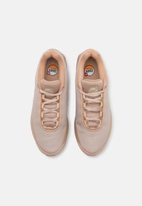 Beige athletic shoes with a mesh upper, textured surface, and minimalistic design. Features a padded tongue and matching laces.