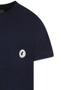 T-shirt di cotone blu navy con collo rotondo e maniche corte. Presenta un logo circolare bianco con la silhouette di un'anatra nera sul petto.