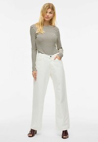 Blusa de manga larga a rayas en beige y negro, combinada con pantalones de pierna ancha blancos. Los zapatos son de color marrón oscuro con un diseño de punta abierta.