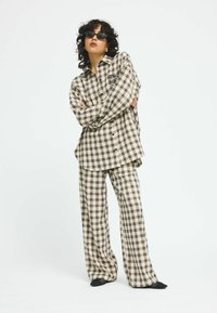 Beige and brown plaid shirt with black buttons and pocket, paired with matching loose-fit plaid pants. Both garments have a relaxed texture.