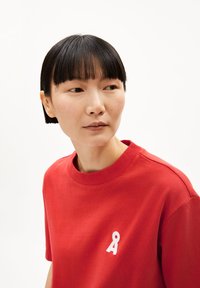 T-shirt di cotone rosso con collo rotondo, maniche corte e un piccolo logo bianco sul petto. Texture liscia e design casual.