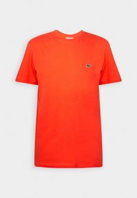 T-shirt rouge uni à manches courtes et col rond avec un petit logo crocodile vert sur la poitrine gauche.
