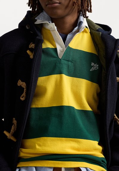 Geel en groen gestreepte rugbyshirt met een V-hals ontwerp en logo, gedragen onder een donker jasje met knopen.