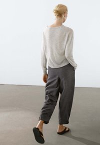 Lichtgrijze top met lange mouwen en losse, donkergrijze broek. De broek heeft knopen bij de boorden en het model draagt zwarte sandalen.