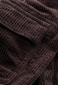 Brun kordflortyg med vertikalt ribbad textur, med mjuka, plyschiga fibrer som skapar ett rikt, taktilt utseende. Kanten är snyggt avslutad.