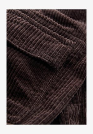 Ruda kordūrinė medžiaga su vertikaliais raukšlėmis, minkštos, pūkuotos skaidulos sukuria turtingą, taktilų išvaizdą. Kraštai tvarkingai apdirbti.