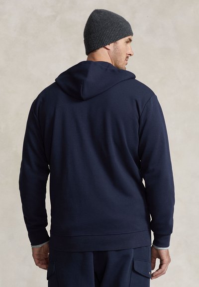 Námořnicky modrá pulovrová mikina s kapucí se stahovací šňůrkou. Měkká látka, pružné manžety a lem. Nositelná s tmavě šedou pletenou čepicí.