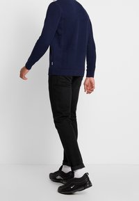 Pull en maille bleu marine avec texture côtelée, jean noir, et baskets Nike Air Max 97 noires avec logo blanc et accents gris.