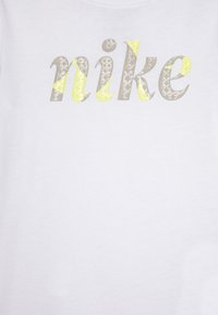 Camiseta blanca con la palabra "nike" en una combinación de colores gris y amarillo brillante, con un patrón texturizado en las letras.