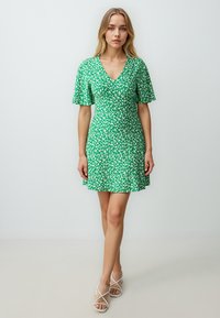 Groene bloemenjurk met een V-hals en korte uitlopende mouwen, gemaakt van zachte stof. Heeft een getailleerd lijfje en een uitlopende rok.