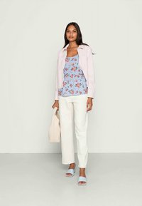 Camisa rosa clara de botão, top peplum azul com flores, calças brancas de perna larga, sandálias azuis claras tipo slide e uma mala tote bege.