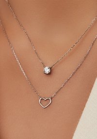 Zilveren gelaagde halskettingen met een kleine hartpendant en een enkele ronde cubic zirconia, beide op delicate kettingen.