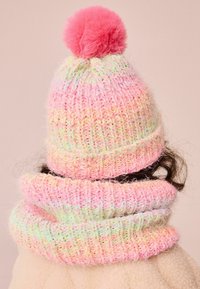 Gebreide muts en sjaal in pastelkleuren, met een pluizige roze pompon, een textuurpatroon en een zachte, gezellige uitstraling.