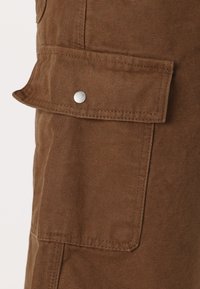 Bruna cargobyxor med en stor fällficka som är säkrad med en metallknapp, tillverkade av slitstarkt texturerat tyg.