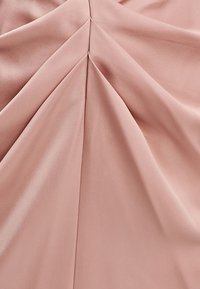 Pink fabric featuring draped pleats, smooth texture, and a soft sheen, creating a fluid and dimensional appearance.