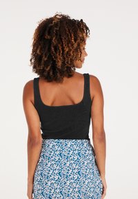 Zwarte geribbelde tanktop met brede schouderbanden, met een vierkante halslijn, gecombineerd met een rok met een bloemenpatroon in blauw en wit.