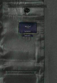 Doublure intérieure d'une veste de costume sombre taillée sur mesure avec un bouton et des étiquettes indiquant "tailored MNG" et "super slim fit."