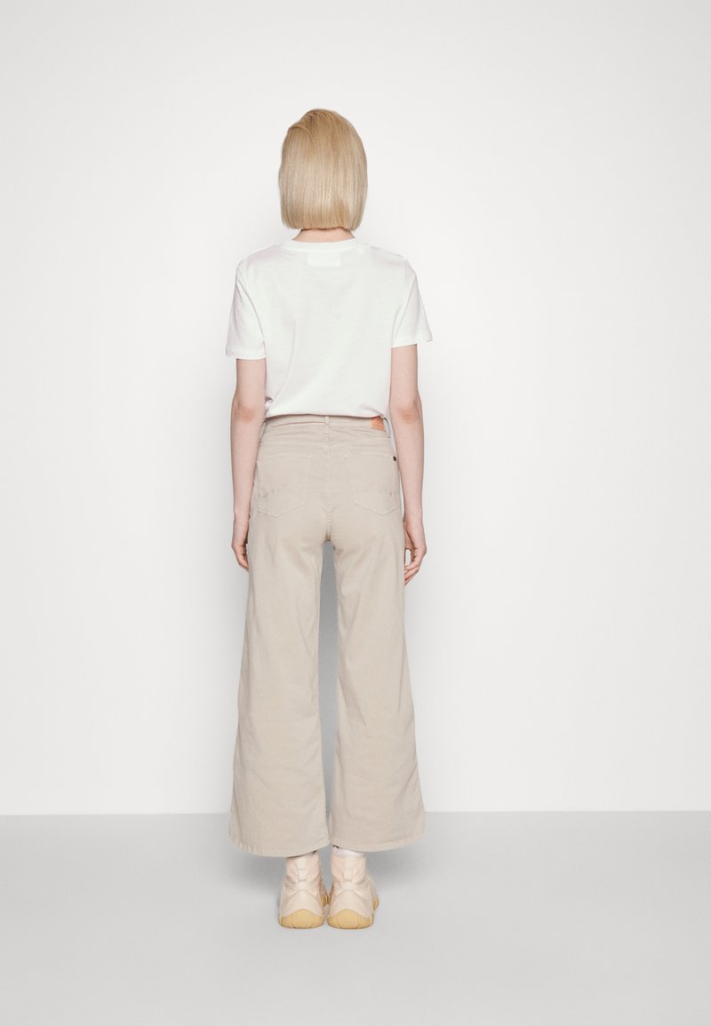 T-shirt bianco in cotone e pantaloni a gamba larga beige chiaro, con tasche posteriori, abbinati a scarpe di colore chiaro. Design semplice e privo di decorazioni.