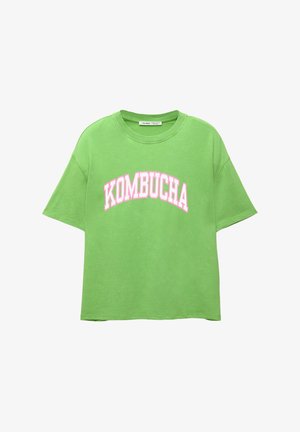 Groene katoenen t-shirt met een relaxte pasvorm, ronde halslijn en korte mouwen. Heeft de tekst "KOMBUCHA" gedrukt in dikke roze letters over de voorkant.