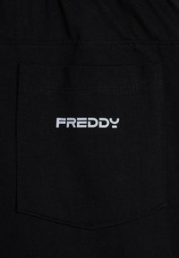 Tessuto nero con finitura testurizzata, caratterizzato da una tasca posteriore. La tasca presenta un logo "FREDDY" stampato in bianco.