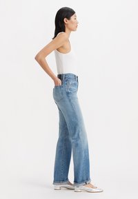 Jeans de mezclilla de corte recto, de talle alto y color azul claro. Cuenta con bolsillos frontales y un acabado desgastado. Combinado con una camiseta sin mangas blanca.