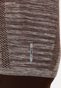 Brązowa, strukturalna koszulka sportowa z poziomymi i kropkowanymi wzorami, z metką logo "ACTIBREEZE" po lewej stronie.